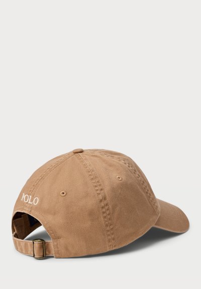 Brūna beisbola cepure ar izliekto mali, ar auduma tekstūru un regulējamu aizmugurējo siksniņu. "POLO" logo izšūts baltā krāsā uz sāna.