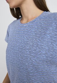 Striped blue and white short-sleeve shirt with a round neckline. Fabric has a soft texture with horizontal lines evenly spaced.