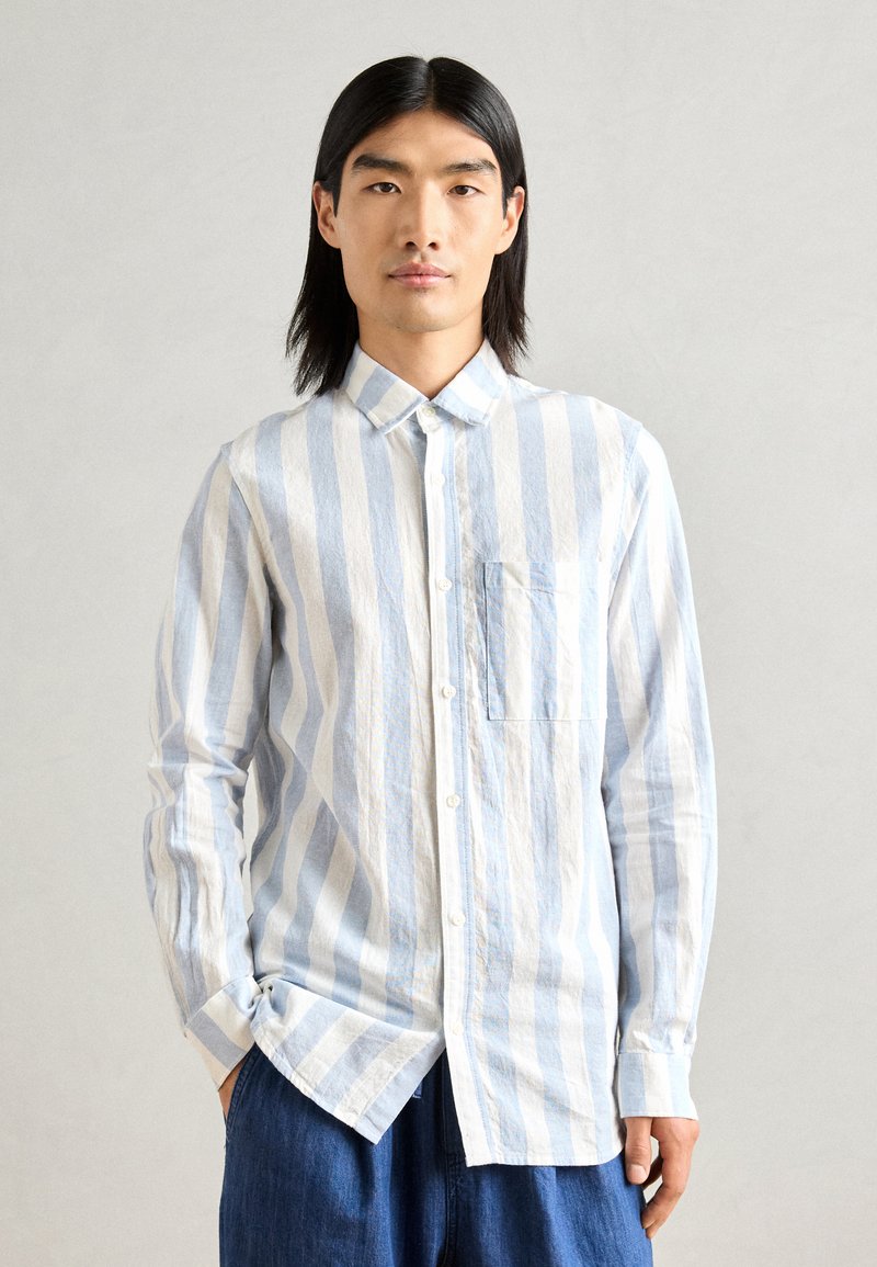 Chemise boutonnée rayée bleu clair et blanche avec un col, une poche poitrine et des manches longues, fabriquée à partir d'un tissu texturé.
