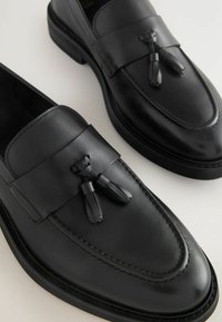 Crne kožne loferice s elegantnim dizajnom, zaobljenim vrhom, šivanim detaljima i resicama sprijeda. Gumeni potplat za dobar grip.