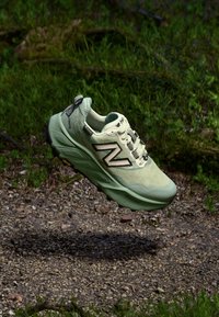 Lichtgroene hardloopschoen met een bovenwerk van gestructureerde stof, zwarte accenten en een gedempte zool. Voorzien van een opvallend "N"-logo aan de zijkant.