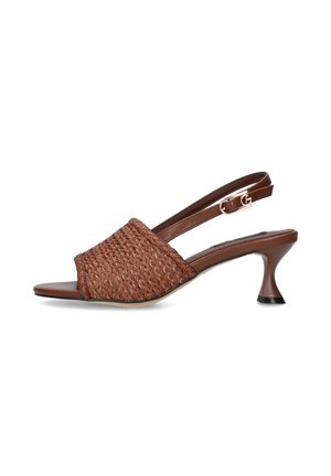 Sandalo marrone intrecciato open-toe con cinturino regolabile con fibbia e tacco kitten curvo su sfondo bianco.