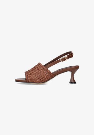 Sandalo marrone intrecciato open-toe con cinturino regolabile con fibbia e tacco kitten curvo su sfondo bianco.