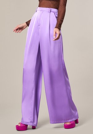 Pantalons larges en satin lilas avec des plis, dotés d'une taille haute et d'une texture lisse. Associés à des sandales à plateforme roses.