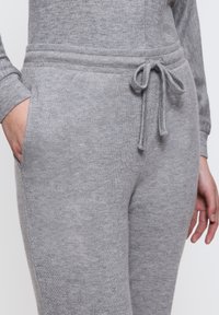 Grå joggers i mjukt tyg med dragsko i midjan, med sidofickor och en åtsittande design. Slät textur med minimal detaljering.