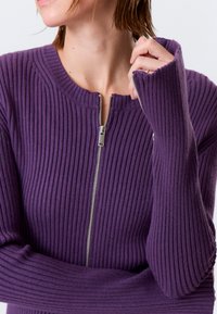 Pull violet côtelé avec un col montant et des manches longues. Doté d'une fermeture éclair frontale avec une quincaillerie argentée. Texture paraît douce.