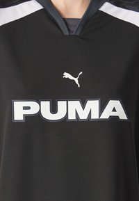Czarny sportowy podkoszulek z dekoltem w serek, z dużym białym logo "PUMA" oraz skaczącym ikoną pumy. Teksturowana tkanina z białymi akcentami na ramionach.