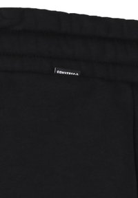 Tissu de coton noir avec une texture lisse, doté d'une taille élastique et d'une petite étiquette blanche "CONVERSE" cousue sur le côté.