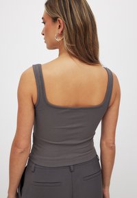 Hall muidud triipudega tank top laia rihmaga ja ruudukujulise kaelusega, millel on tihe ja siledat tekstuuri. Ideaalne kihtide jaoks või casual riietuseks.
