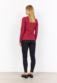 Long-sleeve shirt in red and dark pink stripes, fitted design. Paired with black skinny jeans and flat, textured black shoes.