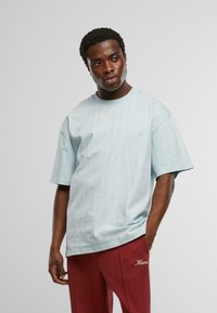 Gaiši zila īsām piedurknēm T-krekls ar plānām vertikālām svītrām un apaļu kakla izgriezumu. Uz krūtīm ir neliels logo. Viegla kokvilnas auduma apdare.