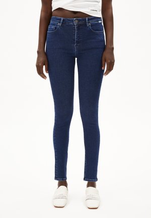 Skinny jeans in donkerblauwe denim, high-waisted met een soepele textuur, met voorzakken en een enkele achterzak als detail.