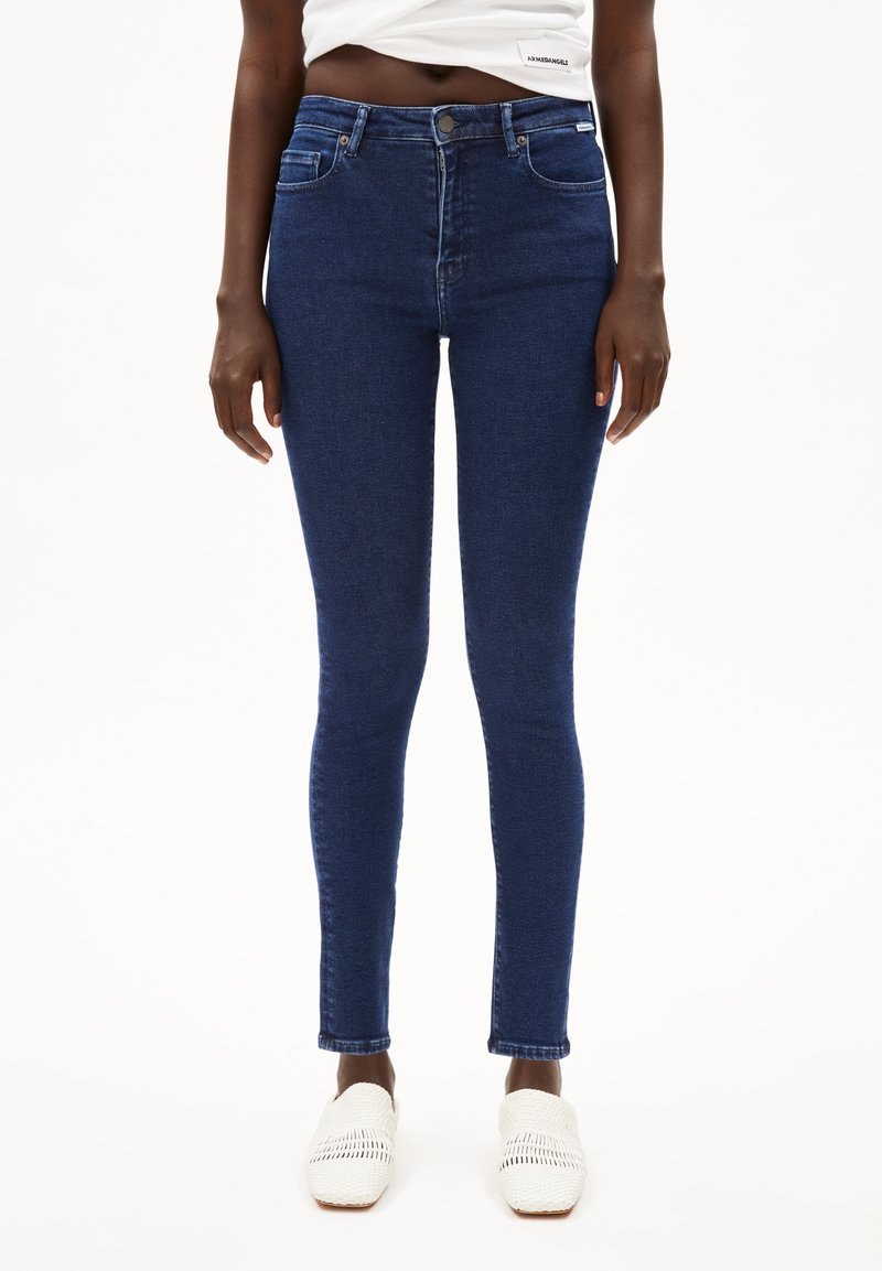 Jean skinny en denim bleu foncé, taille haute avec une texture lisse, présentant des poches avant et un détail de poche arrière.