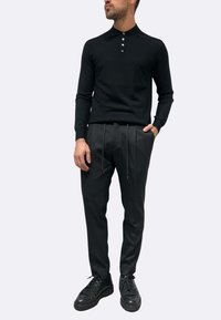 Maglione nero a maglia con colletto polo e tre bottoni. Abbinato a pantaloni neri su misura con coulisse e gambe affusolate. Sneakers nere.