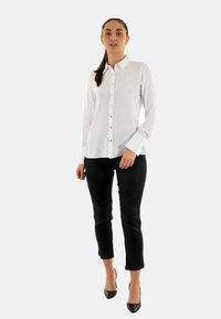 Camisa blanca de botones con una textura suave, con un cuello puntiagudo y botones dorados, combinada con pantalones negros ajustados y tacones.