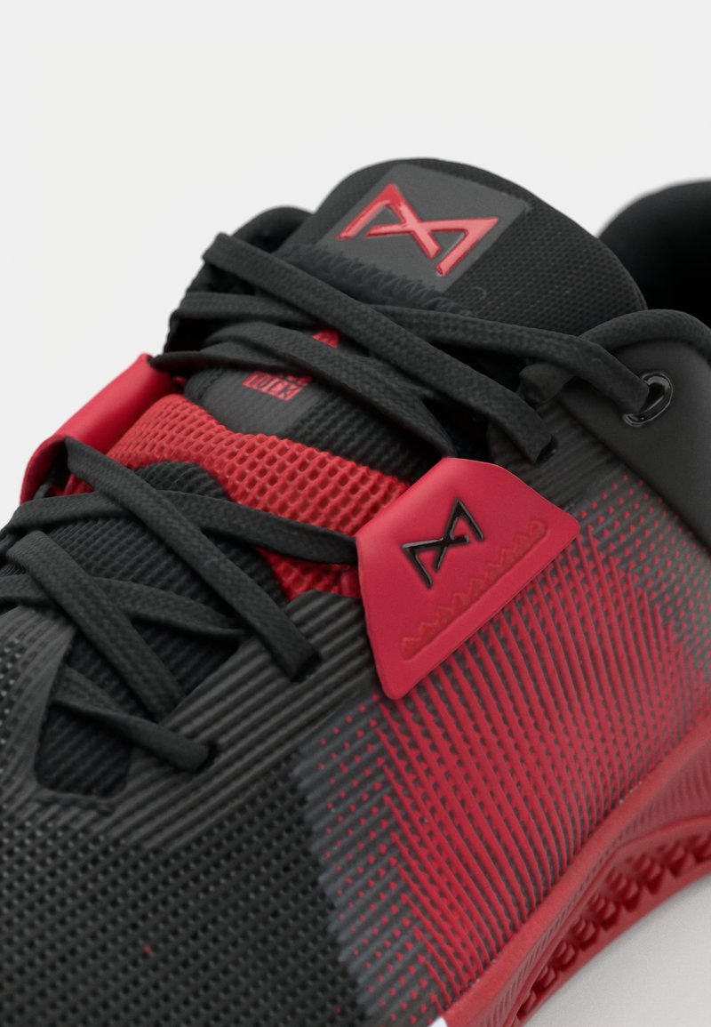 Zapatilla deportiva para hombre con parte superior de malla negra y roja, patrón texturizado, suela de goma y acentos de logo en la lengüeta y ojales.