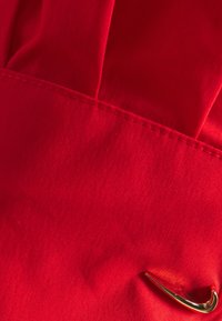 Tela roja con una textura suave y un brillo sutil, que presenta un prominente logo de Nike en color dorado. Se pueden ver los bordes cosidos.