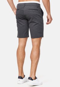 Shorts gris en tissu texturé, dotés de deux poches arrière et d'une ceinture blanche, associés à des baskets blanches avec des détails bleu marine.