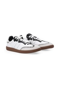 Białe skórzane sneakersy z czarnymi akcentami, szczegółowym teksturowanym przeszyciem, płaskimi białymi sznurowadłami i brązową gumową podeszwą. Niski krój.