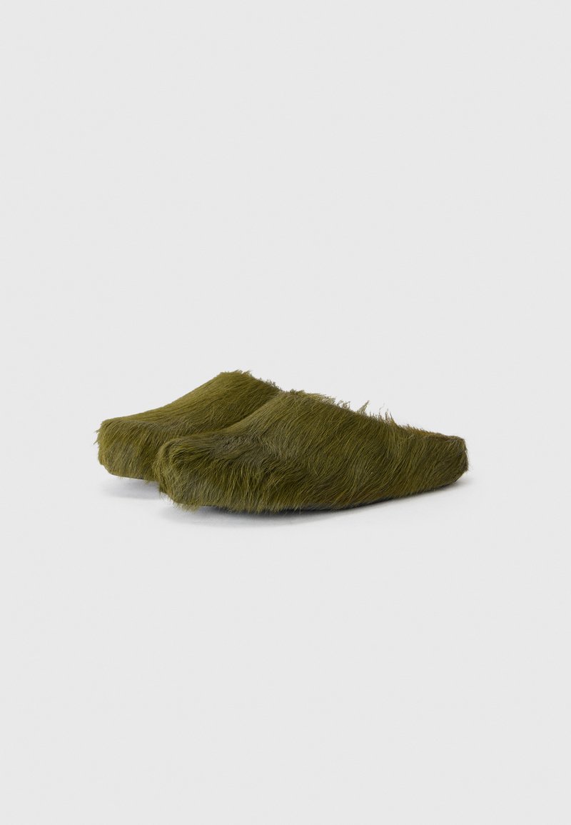 Zoccoli verde oliva pelosi con forma arrotondata, caratterizzati da una superficie texturizzata e pelosa e un design semplice. Nessun hardware o accento visibile.