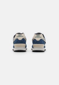 Navy blue suede and mesh sneakers with beige accents. Feature raised heel, smooth sole, and "New Balance" logo at the back.