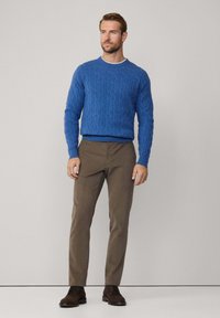Suéter azul de punto trenzado, pantalones marrones a medida y zapatos marrones. El suéter tiene puños y dobladillo acanalados, con un cuello redondo y un patrón texturizado.