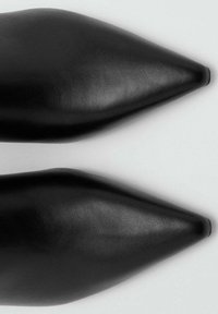Zapatos negros de punta afilada con un acabado de cuero suave, diseño elegante y forma cónica. Sin adornos ni herrajes visibles.