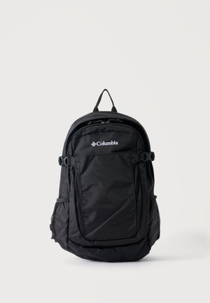 Mochila negra Columbia con bolsillo frontal con cremallera, bolsillos laterales de malla, asa superior y correas ajustables sobre fondo claro y liso.