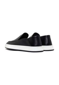 Black slip-on sneakers with a textured leather upper, white rubber sole, and minimalistic design featuring a smooth finish and subtle accents.