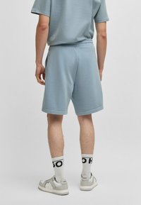 Shorts en coton bleu clair avec une taille élastique, associés à des chaussettes blanches avec des inscriptions noires et des chaussures de sport grises.