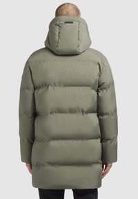 Jachetă umplută de culoare verde măslinie, cu glugă, având un buzunar pe spate cu fermoar și un model matlasat. Textură netedă, lungime până la mijlocul coapsei.