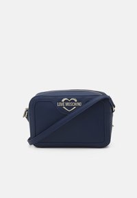 Námořnická modrá crossbody taška Love Moschino s výšivkou zlatého srdce, obdélníkový tvar a nastavitelný popruh na bílém pozadí.