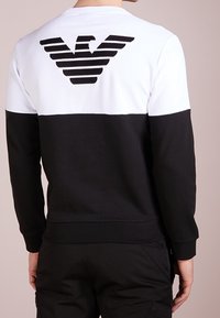 Black and white sweatshirt featuring a horizontal color block design, round neck, and a striped logo on the back, made from soft fabric.