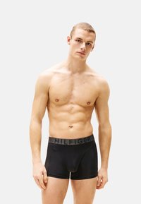 Boxers negros con una cinturilla gris que presenta la inscripción en relieve "HILFIGER". Textura suave, diseño ajustado y largo hasta el muslo.