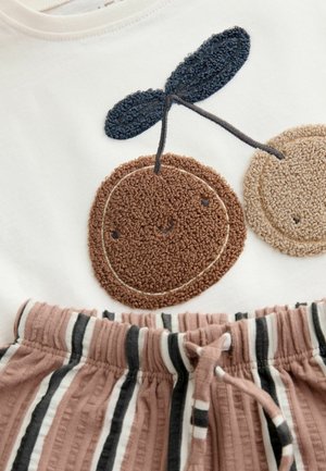 Biele tričko so strapcovou výšivkou čerešní v hnedej a béžovej farbe; krátke nohavice z pruhovanej látky v hnedej a bielej farbe s elastickým opaskom.