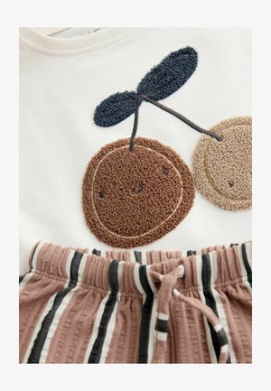 Balta T-krekls ar brūnu un bēšu pūkainu ķiršu izšuvumu; brūni baltas svītras audums šortiem ar elastīgu vidukļa jostu.