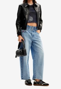 Svart läderjacka i cropped modell, genomskinlig marinblå topp, ljusblå högmidjade vida jeans, svart handväska och svarta sneakers med vita accenter.