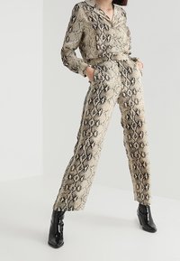 Beżowy i czarny strój w wzór wężowy z koszulą na długi rękaw z kołnierzykiem oraz wysokim stanem spodni. Cechuje się gładką teksturą i luźnym krojem.