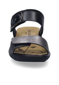 Zwarte leren sandaal met een brede band en een verstelbare gesp. Voorzien van een gevormde tan binnenzool met bladvormen. Vlakke zwarte buitenzool.