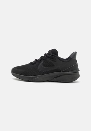 Zapatos deportivos negros con un upper texturizado, puntera redondeada y un tacón ligeramente elevado. Cuenta con un prominente logo de swoosh y diseño de cordones.