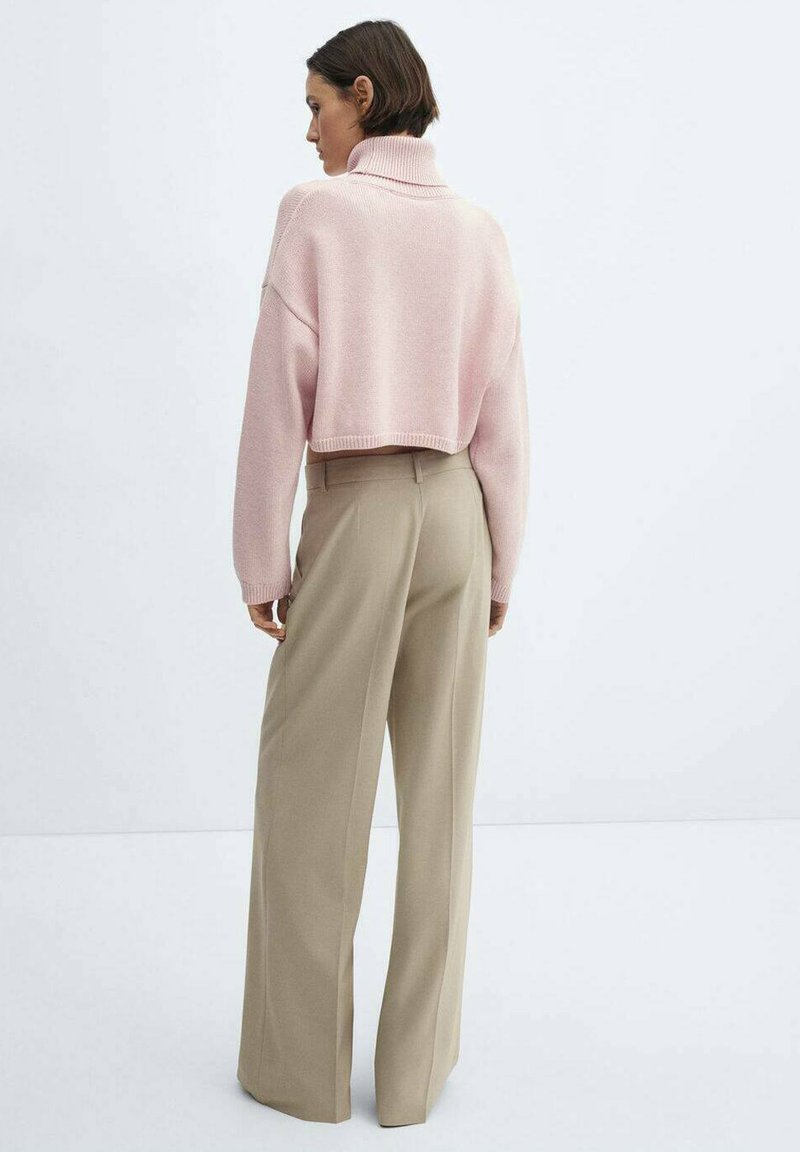 Rosa, kurzes Sweatshirt mit hohem Kragen, kombiniert mit beigen, weiten Hosen. Die weiche Textur, das Strickmuster und die lockere Passform betonen den Komfort.