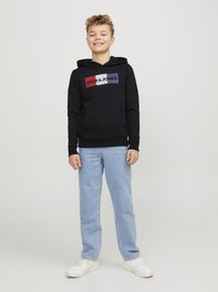 Felpa nera con cappuccio caratterizzata da un logo multicolore sulla parte anteriore, abbinata a jeans dritti azzurri chiari e sneakers bianche.
