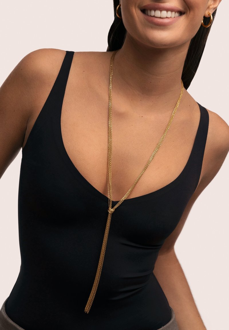 Collar de cadena dorada con un diseño texturizado que cuelga en forma de Y en capas, llevado sobre una camiseta sin mangas negra.