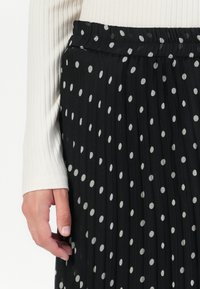 Gonna nera plissettata con pois bianchi, dotata di una vita elastica, abbinata a un top a maniche lunghe color crema a costine.