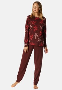 Bordeaux loungewear set met een langekoots top met rode en lichtroze bloempatronen en bijpassende, loszittende broek. Zachte textuur.