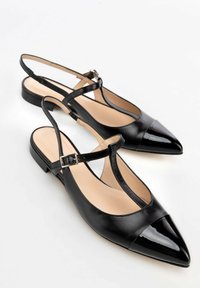 Zapatos de piel negra tipo slingback con punta afilada, que presentan una puntera de charol brillante, suela plana y una correa ajustable con un hebilla plateada.