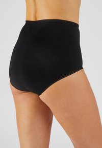 Perizoma nero a vita alta realizzato in tessuto liscio, con bordo scallop lungo la vita e le aperture delle gambe, che offre una copertura totale.