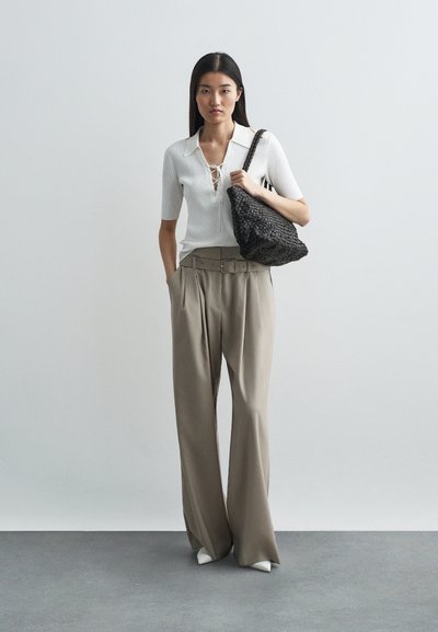 Λευκή ριμπ μπλούζα με λεπτομέρεια δέσιμο, συνδυασμένη με ψηλόμεσα μπεζ παν trousers που διαθέτουν φαρδύ πόδι και ζώνη στη μέση. Συμπεριλαμβάνεται μαύρη πλεκτή τσάντα.