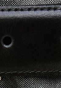 Czarny pasek z czarnej sztucznej skóry z drobnymi detalami szwów i okrągłym otworem, kontrastujący z teksturowanym czarnym tłem materiału.