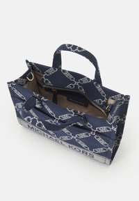 Sac en toile marine avec motif de logo blanc, deux anses supérieures et fermeture éclair. L'intérieur est doté d'une doublure beige avec une poche zippée.